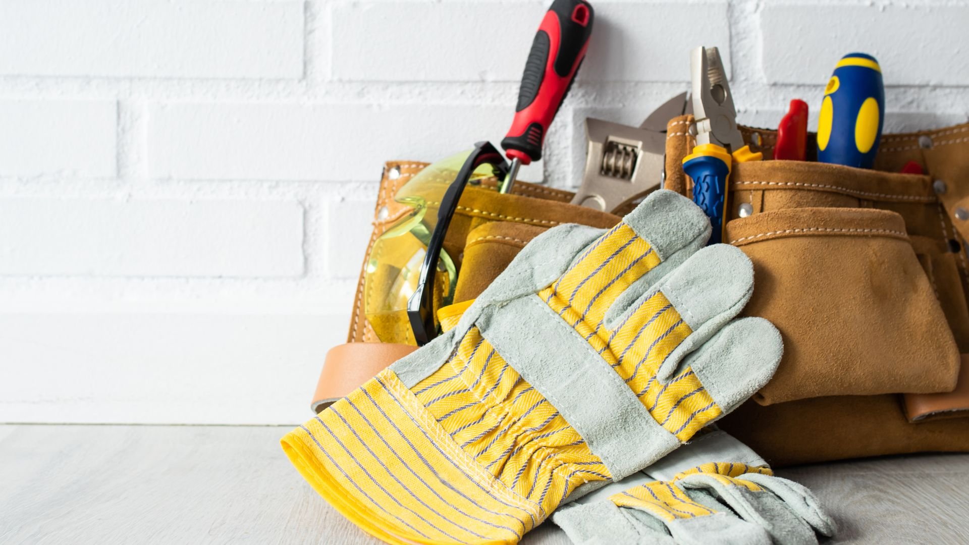 Work gloves and tools in leather tool belt against white brick wall