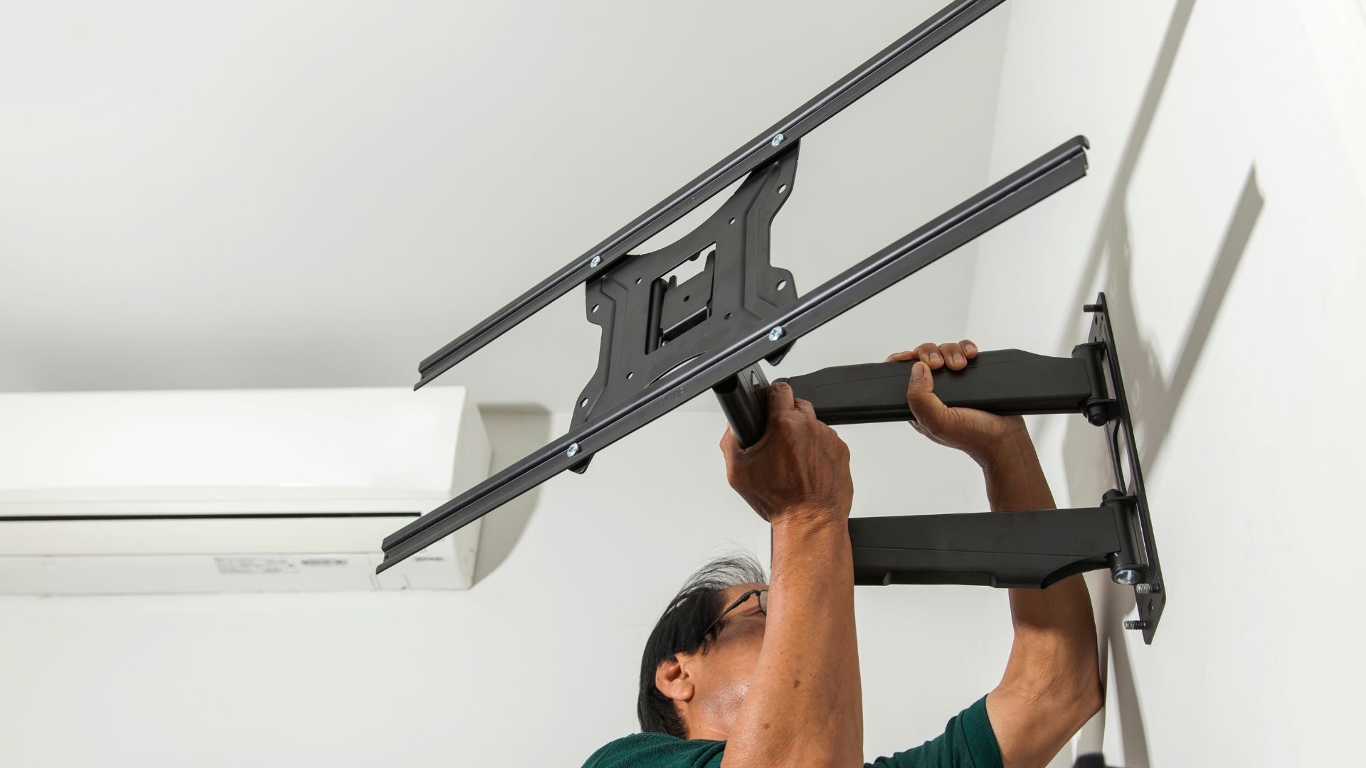 Person installing a large articulating TV wall mount on white wall