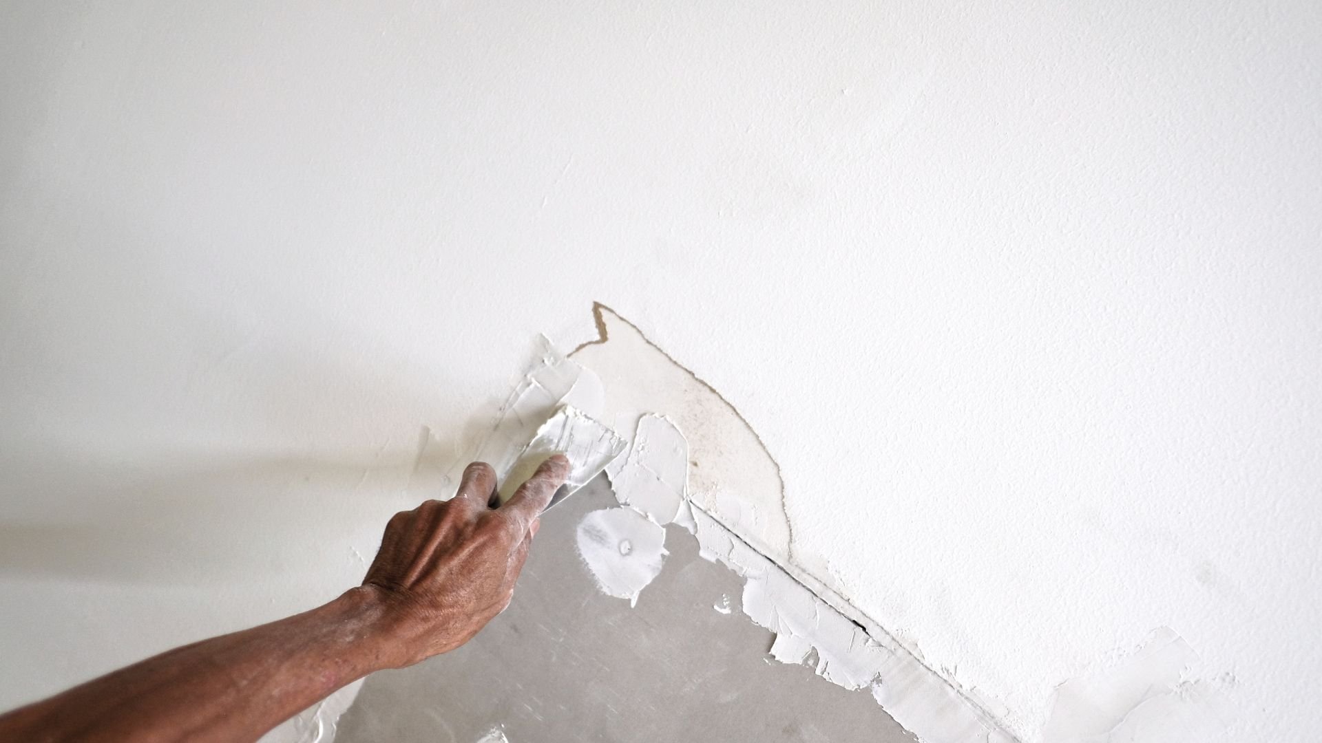 Hand scraping and removing damaged white paint from wall surface