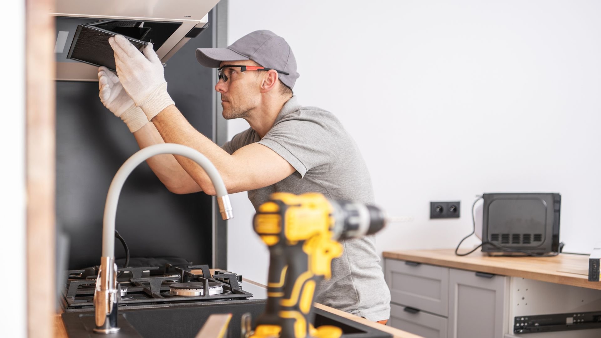 Technician installing kitchen appliance with power drill nearby