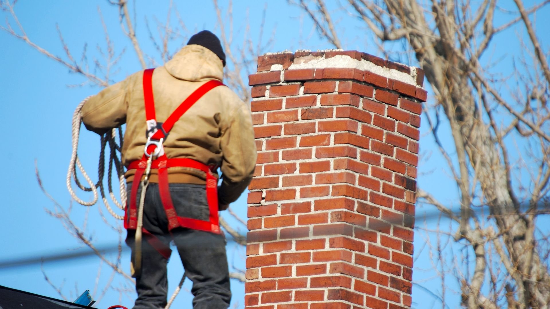 Chimney sweep with safety harness working on brick chimney in winter