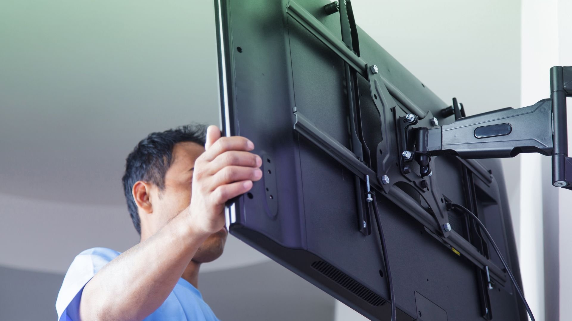 Person mounting a large display screen on an adjustable wall bracket